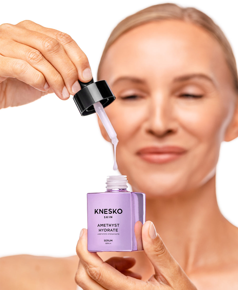 Person applying Knesko Amethyst Hydrate serum to their face with a dropper.