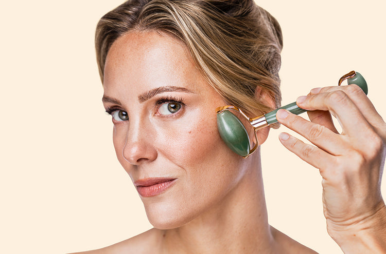 Woman using a jade roller on her face against a beige background