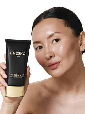 Woman holding a KNESKO Cleanser packaging against a white background