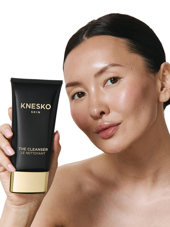 Woman holding a KNESKO Cleanser packaging against a white background