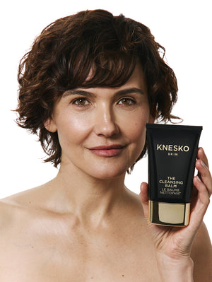Woman holding a KNESKO cleansing balm bottle against a white background