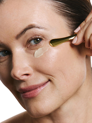 Woman applying eye cream with a applicator on a white background