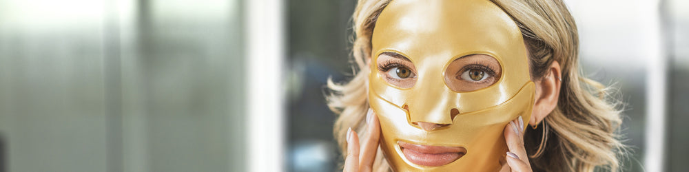 A woman wearing a KNESKO Gold Repair Collagen Face Mask, holding it gently against her cheeks.