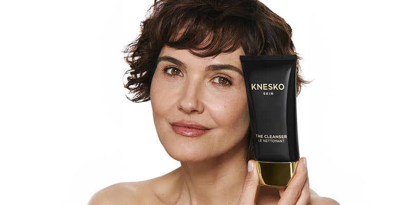 Woman holding a Knesko skincare product against a white background