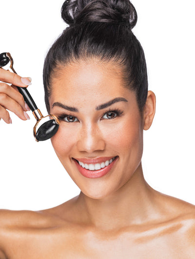 Woman using a black face roller on her face against a white background