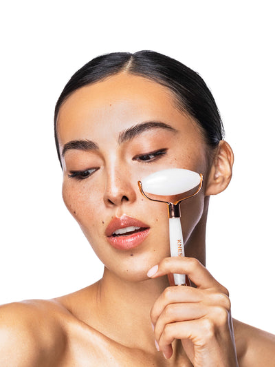 Woman using a white facial roller on her face against a white background
