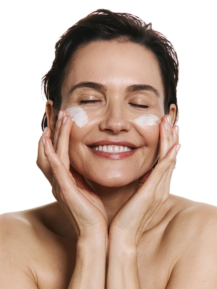 Woman applying product to her face with a white background