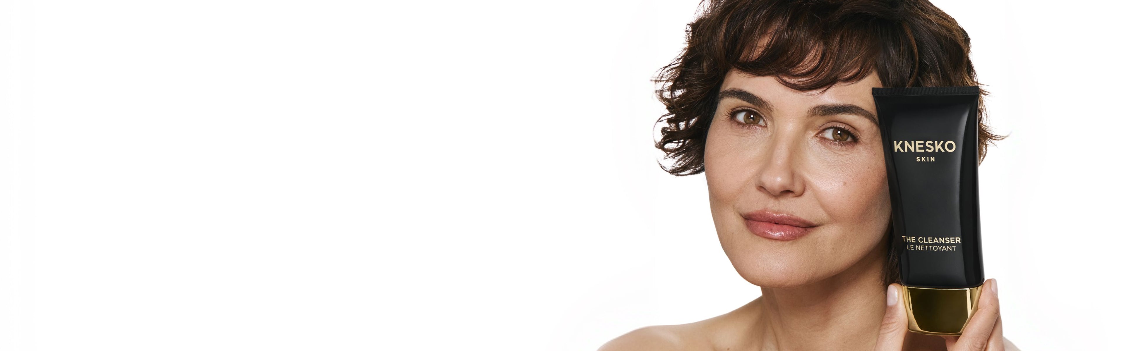 Woman holding a Knesko skincare product against a white background