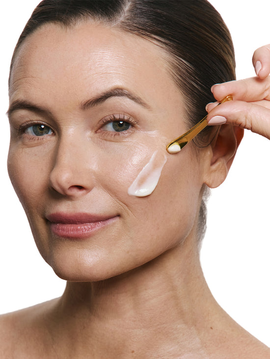 Woman applying cream to her face with a applicator on a white background