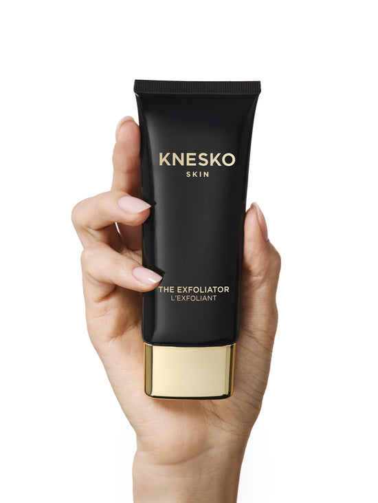 Hand holding a Knesko Skin exfoliator tube against a white background