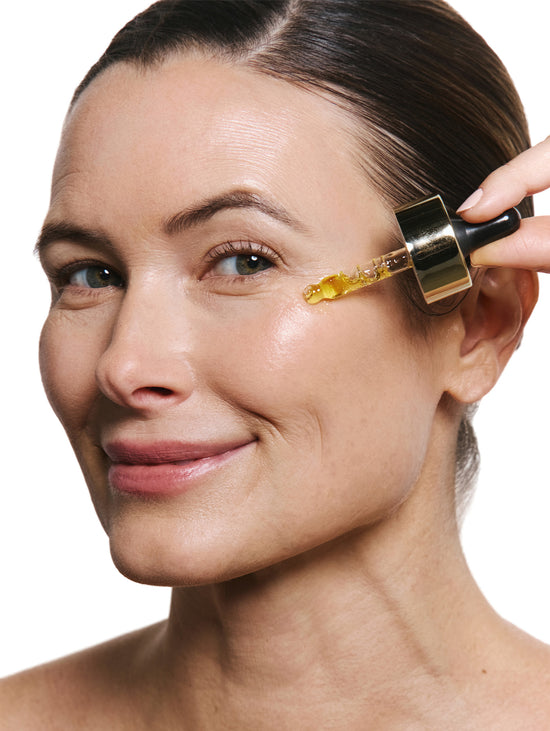 Woman applying a skincare product to her face with a dropper.