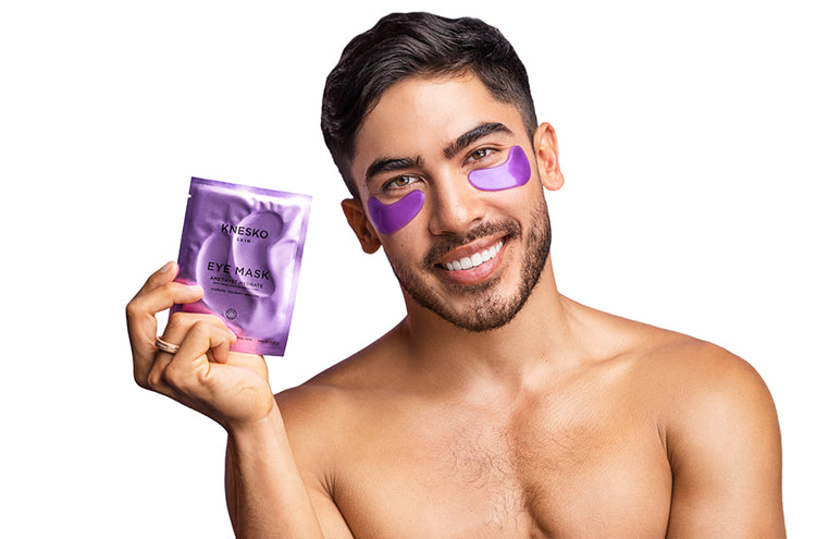 Man wearing purple eye masks holding a KNESKO eye mask package on a white background