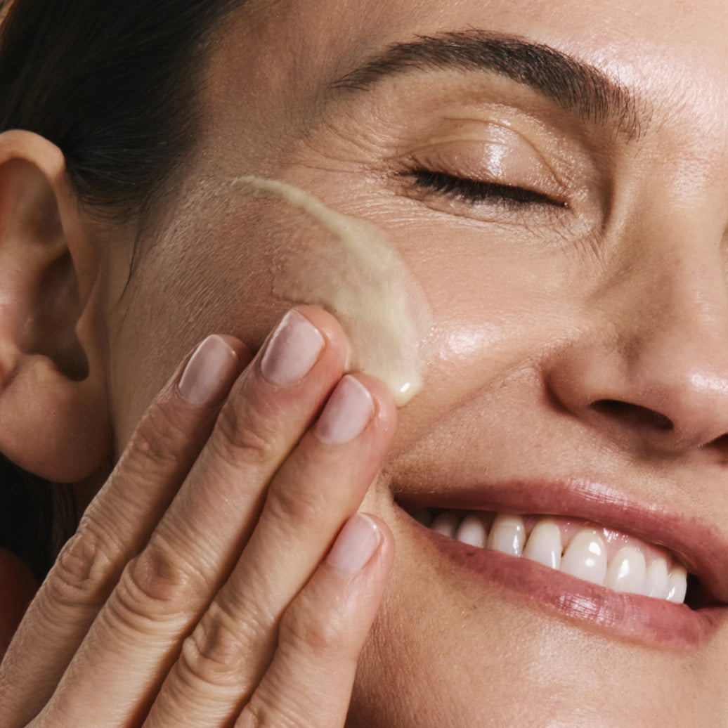 Woman applying product to her face with a close-up view of her hand and cheek.