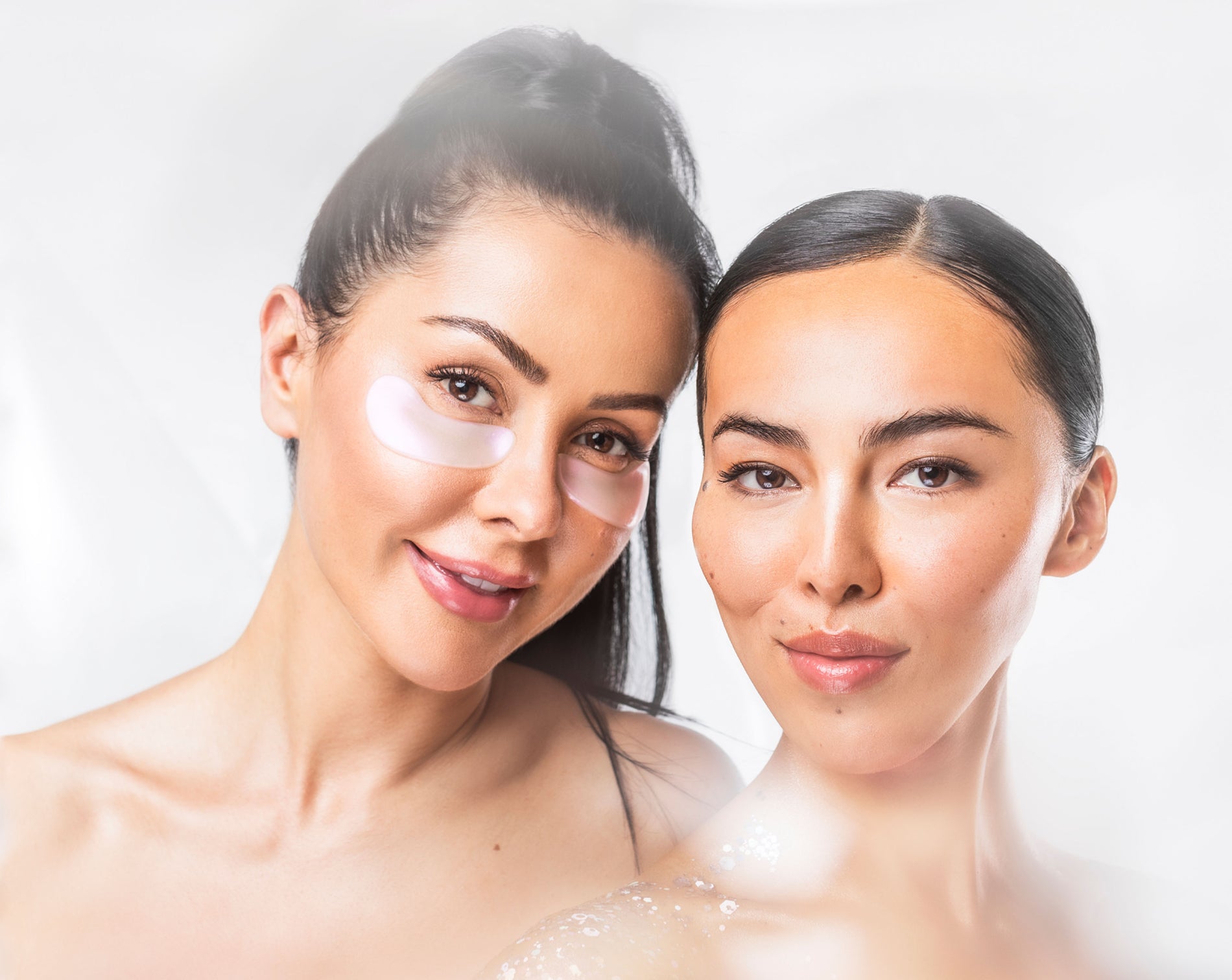 Two women on a white background one is wearing eye masks