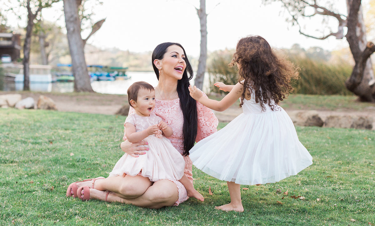 Woman and two young children in pink dresses playing on grass