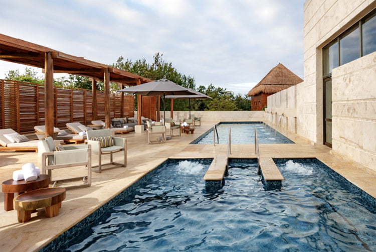 Outdoor pool area with lounge chairs, tables, and a building in the background.