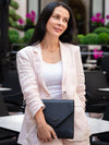 Woman holding a black clutch in an outdoor setting with greenery and pink flowers.