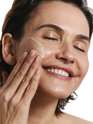 Woman applying product to her face with a white background