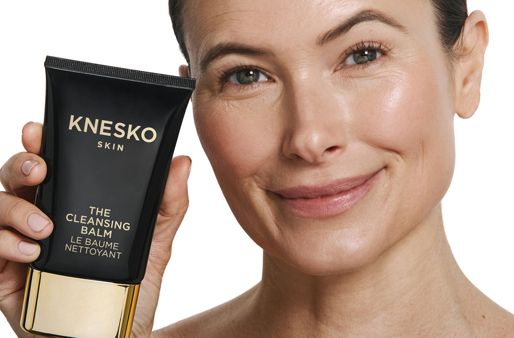 Woman holding Knesko Skin cleansing balm against a white background