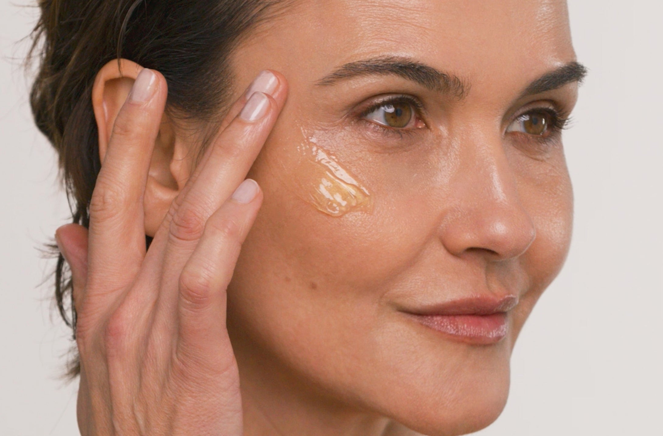 Woman applying product to her face with a neutral background