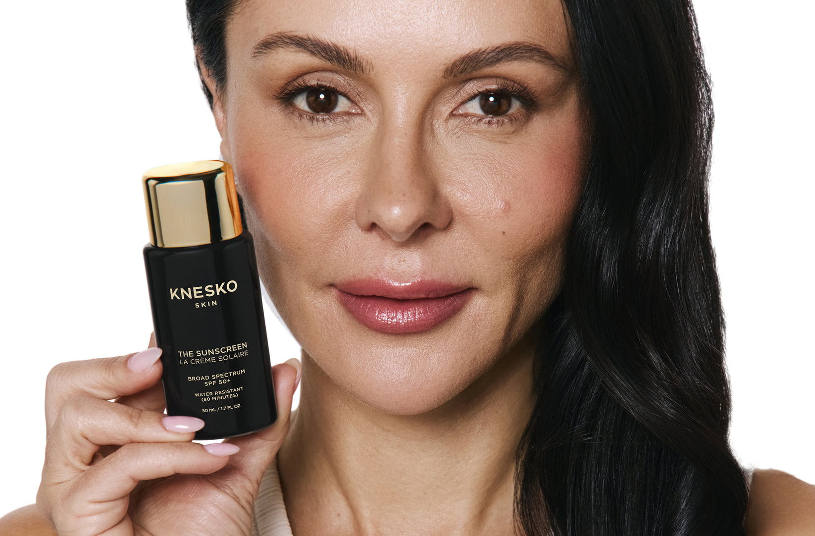 Woman holding a Knesko skincare product against a white background
